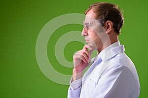 Young man doctor wearing protective glasses against green background