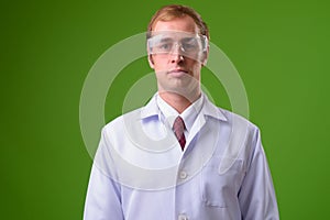 Young man doctor wearing protective glasses against green background