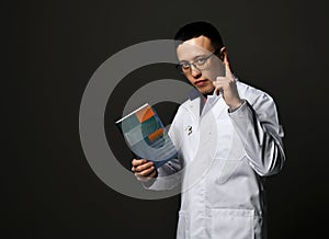 Young man doctors in white medical uniform gown stands holding professional books with blank cover in hand and finger up