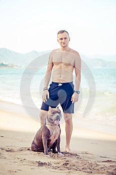 Young man with dog american pit bull terrier posing on the tropical beach