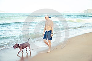 Young man with dog american pit bull terrier walking on the tropical beach
