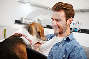 Young Man With Dog Sit On Sofa Using Digital Tablet