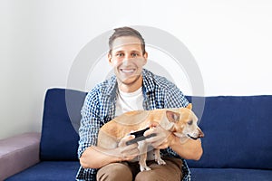 Young man with dog sitting on sofa and holding joystick. Close-up of an attractive bristle guy holding a joystick playing games on