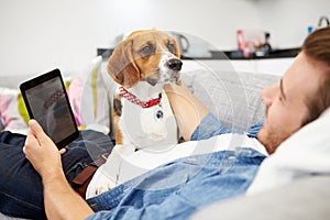 Young Man With Dog Sitting On Sofa Using Digital Tablet