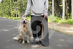 A young man and a dog on a skateboard ride in the park in the summer