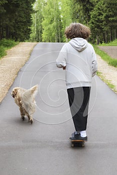 A young man and a dog on a skateboard ride in the park in the summer