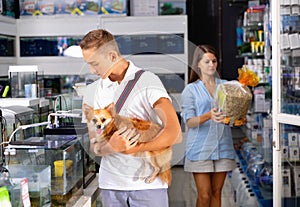 Young man with dog standing near aquarium in pet shop