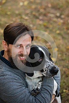 Young man with dog walks in autumn park. He hugged his pet. Dog is hunting, short-footed, lop-eared and spotty. Outbred dog