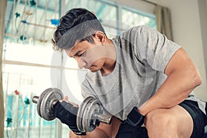 Young man doing exercises biceps with dumbbell on yoga mat in living room at home. Fitness, workout and traning at home concept