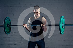 A young man doing exercises with a heavy barbell in the gym