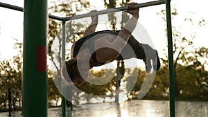 Young man doing exercises outdoors on horizontal bar outdoors. Calisthenics workout on paralel crossbar hanging on arms