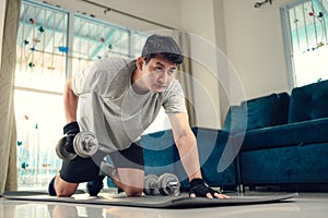 Young man doing exercises triceps muscle with dumbbell on yoga mat in living room at home. Fitness, workout and traning at home