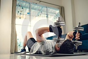 Young man doing exercises triceps muscle with dumbbell on yoga mat in living room at home. Fitness, workout and traning at home
