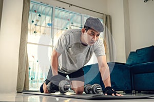 Young man doing exercises triceps muscle with dumbbell on yoga mat in living room at home. Fitness, workout and traning at home