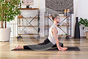 Young man doing Half Pigeon yoga pose on mat