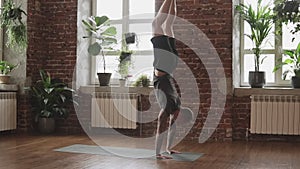 Young man doing hand standing pose. Guy doing yoga indoors near windows