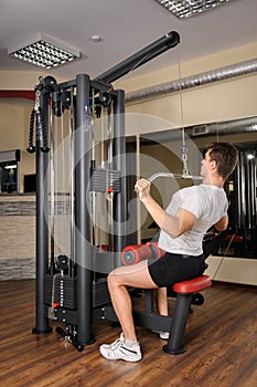 Young man doing lats pull-down workout in gym