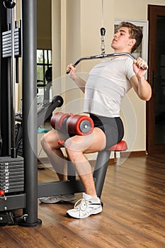 Young man doing lats pull-down workout in gym