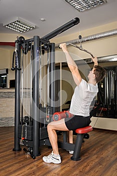 Young man doing lats pull-down workout in gym