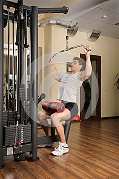 Young man doing lats pull-down workout in gym