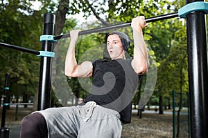 Young man doing pull ups on horizontal bar outdoors, workout, sp