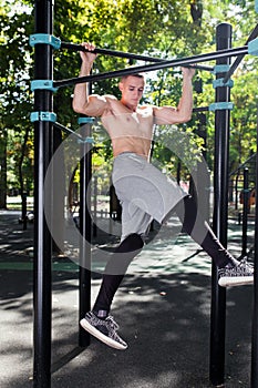 Young man doing pull ups on horizontal bar outdoors, workout, sp
