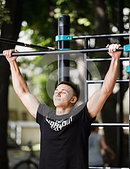 Young man doing pull ups on horizontal bar outdoors, workout, sport concept