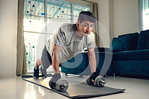 Young man doing push up with dumbbell and exercises on yoga mat in living room at home. Fitness, workout and traning at home