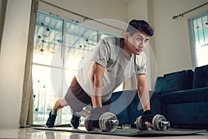 Young man doing push up with dumbbell and exercises on yoga mat in living room at home. Fitness, workout and traning at home photo