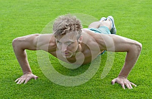 Young man doing push-ups on green grass