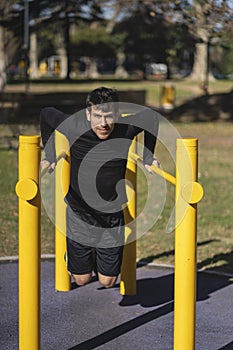 Young man doing push ups on horizontal bar outdoors