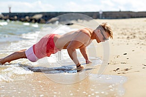 Young man doing push-ups on summer beach