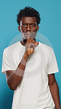 Young man doing silence gesture with finger on mouth