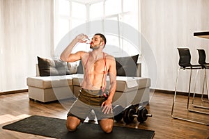 Young man doing sport workout in room during quarantine. Rest after exercise. T-shirtless guy sportsman sit on mat and