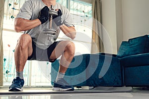 Young man doing squat exercises with dumbbell on yoga mat in living room at home. Fitness, workout and traning at home concept