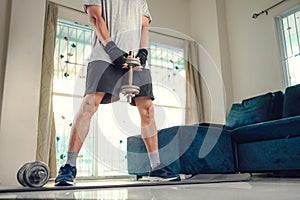 Young man doing squat exercises with dumbbell on yoga mat in living room at home. Fitness, workout and traning at home concept