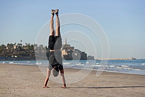 Young man doing yoga exercise - handstand on sandy beach near the sea. Active lifestyle concept.