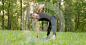 Young man doing yoga pose ina park at morning. Guy doing stretching. Slow motion