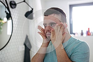 Young man with down syndrome in bathroom, holding his cheeks.