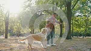 Young man with down syndrome in checkered shirt walking with golden retriever dog outdoors in the park