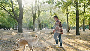 Young man with down syndrome in checkered shirt walking with golden retriever dog outdoors in the park