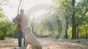 Young man with down syndrome in checkered shirt walking with golden retriever dog outdoors in the park