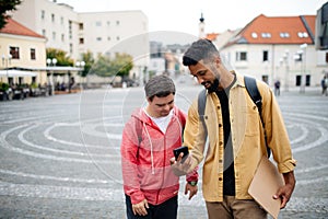 Young man with Down syndrome and his mentoring friend with smartphone walking and talking outdoors