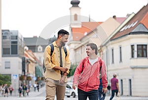 Young man with Down syndrome and his mentoring friend walking and laughing outdoors