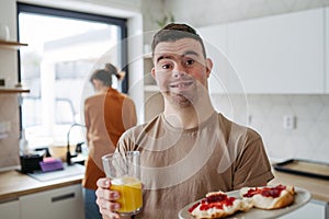 Young man with Down syndrome holding breakfast and glass of juice. Morning routine for man with Down syndrome.