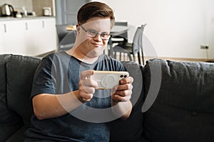 Young man with down syndrome using cellphone while sitting on couch