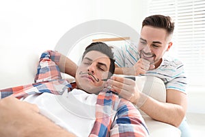 Man drawing mustache on face of sleeping friend indoors. April fool`s day photo