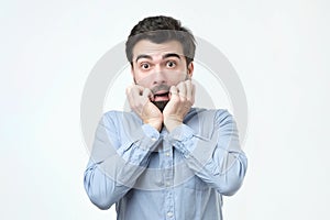 Young man dressed in casual clothes, biting nails and rounding eyes