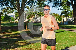 Young man dressed in sportswear runs during training in the park between eucalyptus trees, summer sunny day