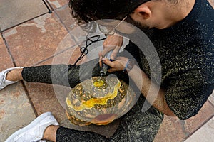 Young man with a drill or dremel drilling a pumpkin for halloween